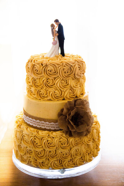 A vertical shot of a yellow wedding cake with couple figures on the top on a white background