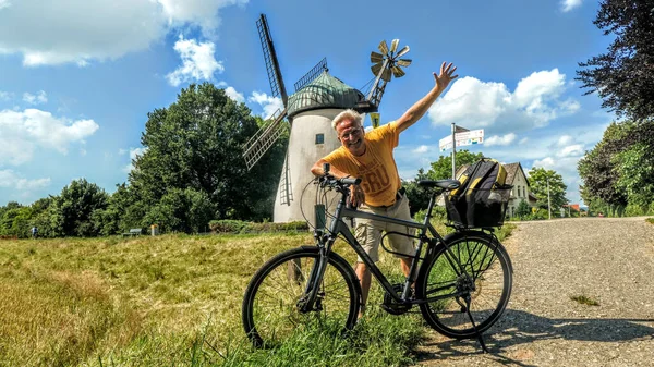 ドイツのヴェーザー サイクル パスの風車の前で喜んでポーズをとる白人のサイクリスト — ストック写真
