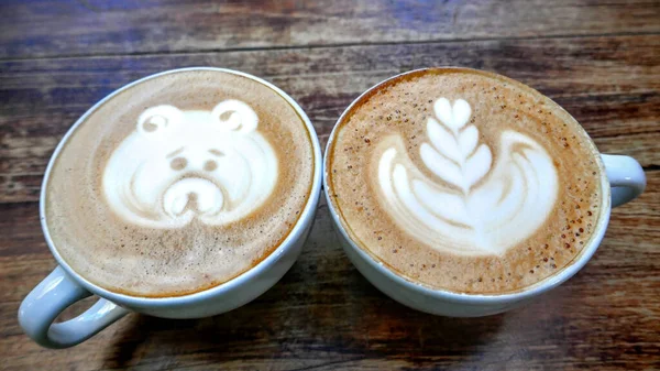 Ahşap bir masaya köpük çizilmiş iki fincan kahvenin açısı..