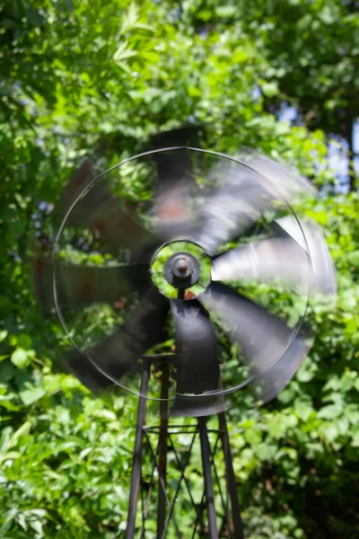 緑の木に対して動作中の古い錆びた風車の垂直ショット — ストック写真