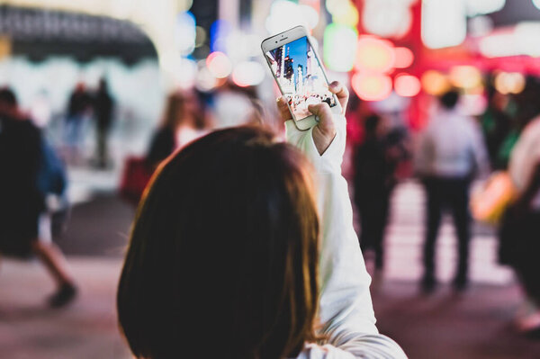 Задний вид женщины, фотографирующей вечерний город с акцентом на телефон