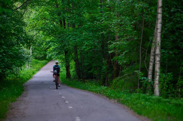 緑豊かな北ヨーロッパの森の道で自転車に乗っている男の子バックパックにサッカーでカメラに向かって後方に直面している — ストック写真