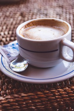 Hasır bir masada bir fincan kahvenin yakın çekimi.