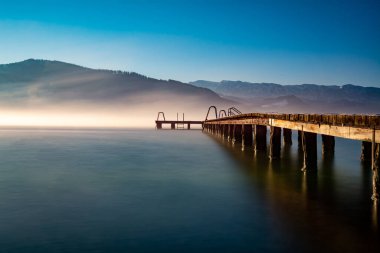 Avusturya 'daki Attersee Gölü' ne giden ahşap bir iskelenin büyüleyici bir görüntüsü. Mavi bulutlu gökyüzü.