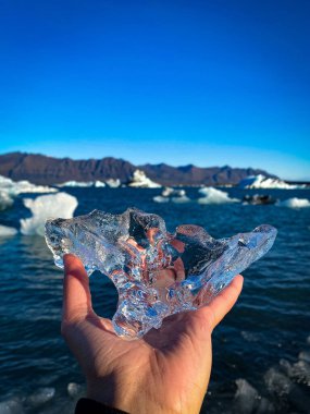 Bir erkek el, deniz manzarasına karşı kristal bir buz parçası tutuyor.