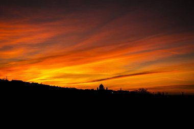Parlak turuncu bir gökyüzünün altında görünen binaların siluetleriyle nefes kesici bir akşam manzarası.