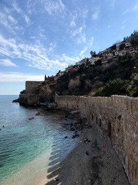 Deniz kıyısında, bulutlu bir gökyüzüne karşı binaları ve ağaçları olan eski bir duvar.