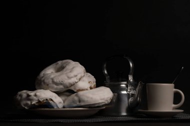 Kahve fincanlı şekerli çörek ve siyah arka planda metal çaydanlık.