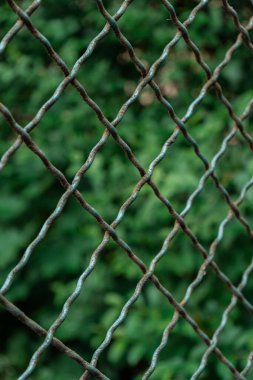 Kırsal alanda bulanık bir zeminde paslı bir çitin dikey görüntüsü.