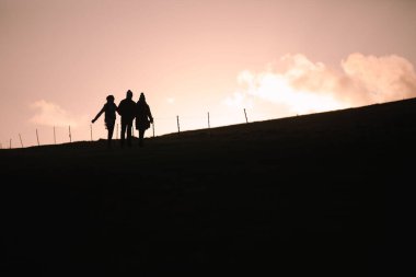 Güney Tepeleri 'nin tepesinde, Doğu Sussex, İngiltere' de üç siluetli insan yürüyor.