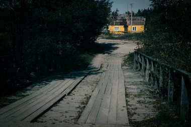 Ağaçlar boyunca sarı bir eve giden ahşap bir patika.