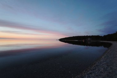 Renkli bir günbatımının arka planındaki taşlı bir sahilin manzarası.