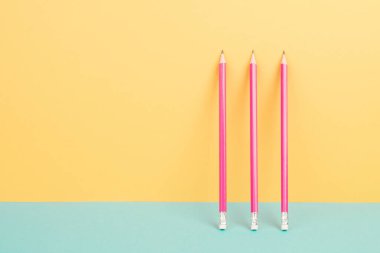 Sarı ve mavi arkaplanda pembe kalemler, minimalizm, yaratıcı, gerçeküstü ve eğitim konsepti, metin için kopya alanı, pastel renkli duvar