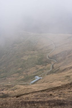 Kırsal bölgedeki tepelerdeki bir binaya giden asfalt yolun dikey görüntüsü.