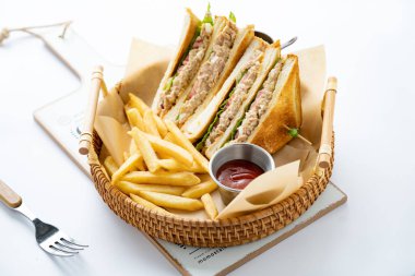 Yanında patates kızartması ve ketçap olan lezzetli bir ton balıklı sandviçe yakın plan.