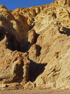 Mavi gökyüzünün altında engebeli bir uçurumun dikey görüntüsü.