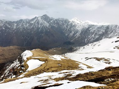 Karla kaplı yamaçlar, karla kaplı dağlar ve arka planda kasvetli bulutlar.