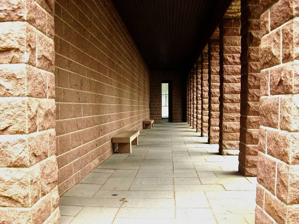 A passage at the side of a building. Banks for sitting down on the left side and pillars on the right side.