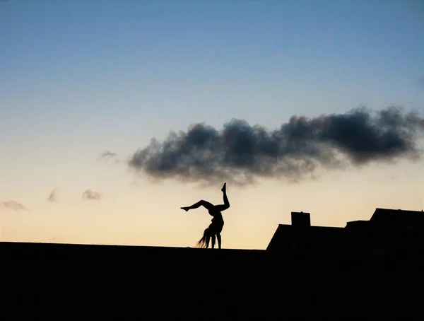 A silhouette of female doing gym on roof in background of clouds
