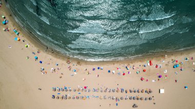 Kumsaldaki insanlarla dolu bir deniz manzarası.
