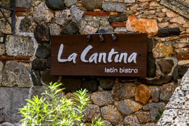 Dominik Cumhuriyeti, Altos de Chavon 'da kayalık bir duvarda asılı duran La Cantana Latin bistrosunun tahta tabelasının yakın plan çekimi.