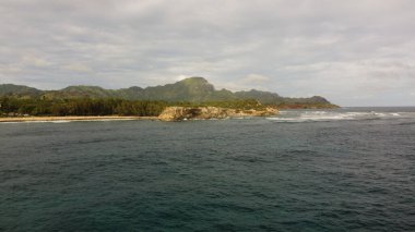 Bulutlu bir günde arka planda kayalık manzaralı güzel bir okyanus manzarası.