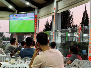 Faslı insanlar bir kafeteryanın terasında futbol maçı izliyor.