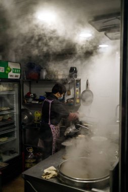 Maskeli aşçının yemek hazırladığı yemek odası mutfağının dikey görüntüsü.