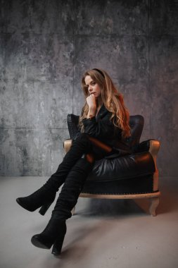 Stüdyoda sandalyede poz veren zarif, koyu renk elbiseli beyaz bir kızın dikey çekimi.