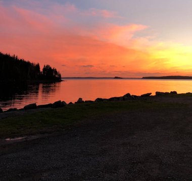 Kırsal bir alanda, canlı bir günbatımı arka planında bir gölün manzarası.