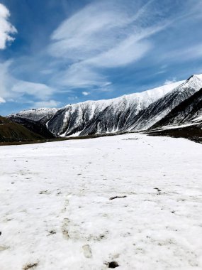 Arka planda bulutlu mavi gökyüzü olan kar kaplı dağların dikey görüntüsü