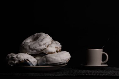 Kahve fincanlı şekerli çörek ve siyah arka planda metal çaydanlık.