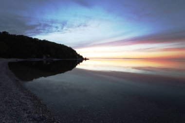 Renkli bir günbatımının arka planındaki taşlı bir sahilin manzarası.