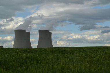 Kırsal kesimde, mavi bulutlu gökyüzüne karşı yeşil bir alanda birkaç soğutma kuleleri var.