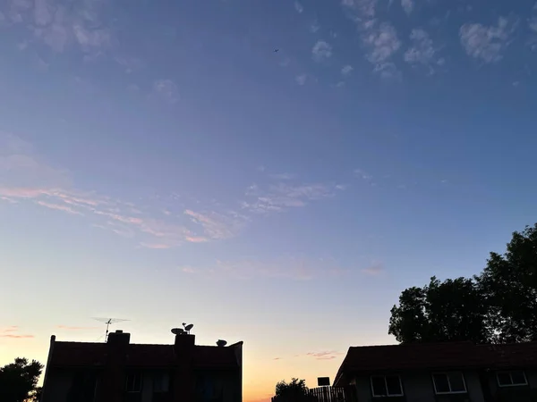 遠くには暗い前景の家とオレンジ色の空の夕日を望む青い空 — ストック写真