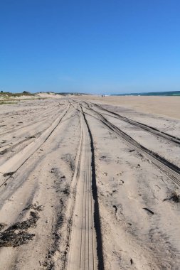 Mavi gökyüzünde tekerlek izleri olan kumlu kıyı şeridinin dikey görüntüsü..