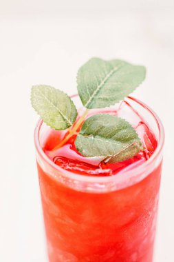 Bulanık arkaplanda buz küpleri ve yeşil yapraklı bir bardak kırmızı içeceğin dikey görüntüsü.