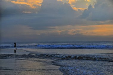 Gün batımında deniz manzarasına karşı kıyıda duran adamın silueti..
