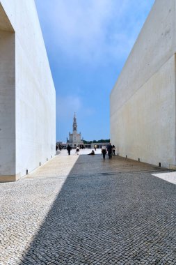 Portekiz, Fatima 'da mavi gökyüzü arka planında beyaz binalarla çevrili bir ara sokağın dikey görüntüsü.