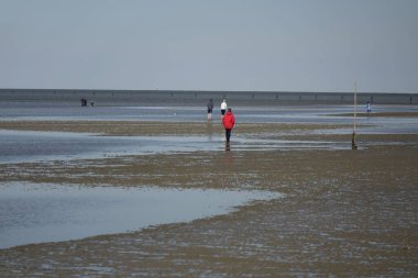 16 Nisan 2022, Sahlenburg, Aşağı Saksonya, Almanya, Kuzey Denizi sahillerinde yürüyen insanlar alçak gelgit, güneşli bahar günü (yatay bahar günü))