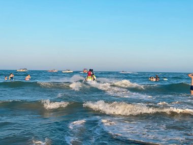 Bir grup insan mavi denizde yüzüyor ve jet ski yapıyor.