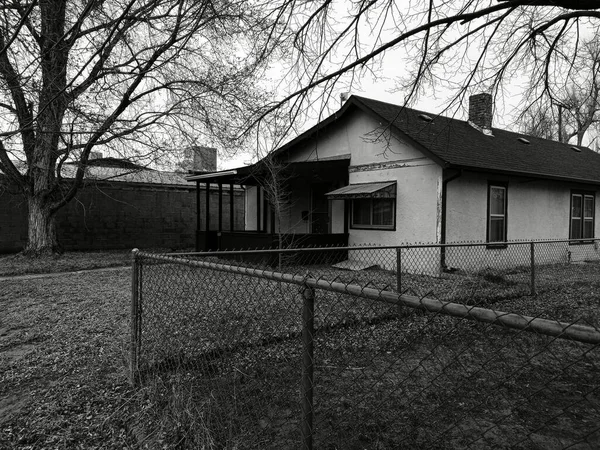 一张灰色的旧房子的照片 房子附近有栅栏和树木 — 图库照片