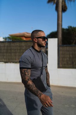 Aynı gömlek ve pantolona sahip genç ve dövmeli bir adamın dikey fotoğrafı.