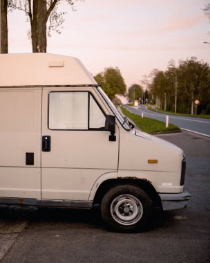 Otobanın yanına park edilmiş eski beyaz bir minibüsün dikey görüntüsü..