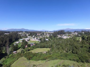 Güneşli bir günde yeşil ormanlarla kaplı tepelerin ve kırsal alandaki evlerin kuş bakışı görüntüsü
