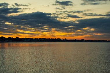 Sakin deniz ve şehrin üzerinde gün batımının manzarası