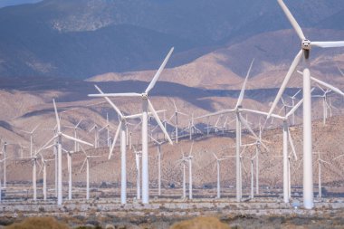 Kırsal kesimdeki dağlara karşı geniş bir arazide rüzgar türbinlerinin doğal bir görüntüsü.