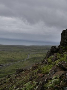 İzlanda 'da bulutlu bir gökyüzünün altında kayalık bir dağ sırasına karşı dikey yeşil alanlar.