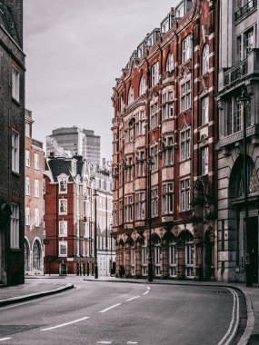 Gri gökyüzüne karşı kırmızımsı binalarla dolu boş bir yolun dikey görüntüsü. Londra, İngiltere.