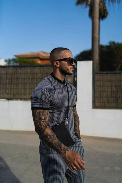 Aynı gömlek ve pantolona sahip genç ve dövmeli bir adamın dikey fotoğrafı.